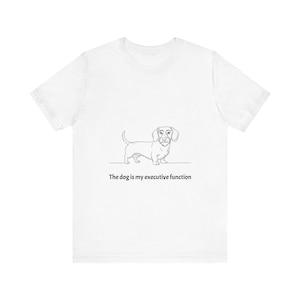 May include: White t-shirt with a simple line drawing of a dachshund. The text below the dog reads: "The dog is my executive function". The shirt is made of a soft material.