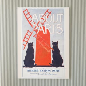 May include: A framed vintage poster titled "About Paris" featuring a red windmill and two black cats. The poster has a light blue background and white text. The author's name is Richard Harding Davis, and the illustrator is C.D. Gibson.