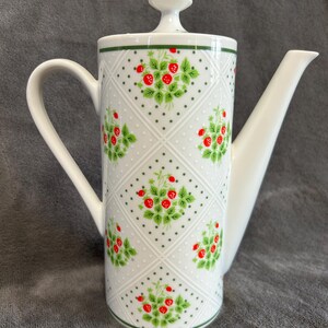 May include: White ceramic coffee pot with a lid and a long spout. The pot is decorated with a pattern of red strawberries and green leaves on a white background. The handle and spout are white, and the rim is green.