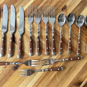 May include: A collection of stainless steel silverware with wooden handles. The set includes knives, forks, and spoons. The wooden handles are a dark brown color with silver rivets. The silverware is arranged on a wooden surface.
