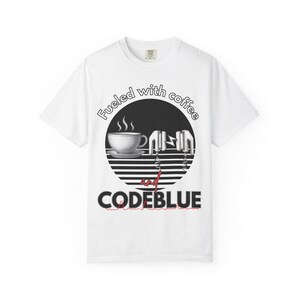 May include: White t-shirt with a graphic design featuring a coffee cup, a mixer, and the text "Fueled with coffee and CODEBLUE." The design is in black and white with red accents. The shirt has a crew neck.
