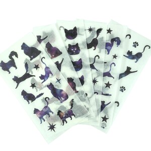 Könnte beinhalten: Blätter mit Aufklebern zum Thema Katze. Die Aufkleber zeigen verschiedene Katzensilhouetten in schwarzen und violetten Galaxiemustern sowie Sterne und Pfotenabdrücke. Die Aufkleber befinden sich auf weißem Hintergrund.