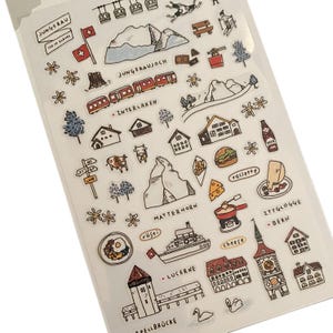 May include: A sheet of stickers featuring Swiss-themed illustrations. Designs include the Matterhorn, Swiss flags, trains, houses, cows, and food items like raclette and rösti. Text includes "JUNGFRAU", "INTERLAKEN", and "LUCERNE".