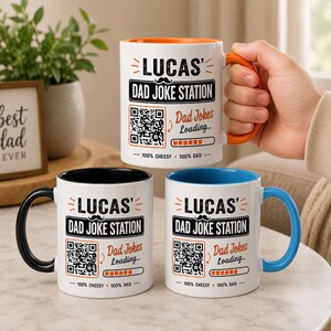 May include: Three white ceramic mugs featuring the text 'LUCAS' DAD JOKE STATION', a QR code, a loading bar, and the text 'Dad Jokes Loading...' and '100% CHEESY 100% DAD'. The mugs have orange, black, and blue interior linings and matching handles.