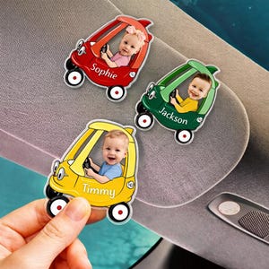 May include: Three colorful car-shaped magnets with smiling babies inside. The cars are red, green, and yellow, each with a different name: Sophie, Jackson, and Timmy. The magnets have white wheels with red centers.