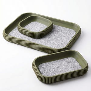 May include: Three-piece tray set in olive green. The trays have a rectangular shape with rounded corners and a ribbed exterior. The interior of each tray features a gray, speckled felt lining. The set includes trays of varying sizes for versatile use.