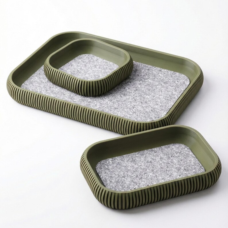 May include: Three-piece tray set in olive green. The trays have a rectangular shape with rounded corners and a ribbed exterior. The interior of each tray features a gray, speckled felt lining. The set includes trays of varying sizes for versatile use.