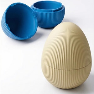 Op de afbeelding: Een eivormige container met een geribbelde textuur in een lichtbeige kleur, naast twee blauwe containers. De blauwe containers hebben een vergelijkbaar geribbeld ontwerp. De eivormige container is gesloten, terwijl een blauwe container open is.