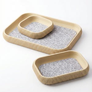 May include: Three wooden trays of varying sizes. The trays have a light brown, ribbed exterior and a gray felt interior. The largest tray is rectangular, with a smaller rectangular tray and a square tray nested inside.