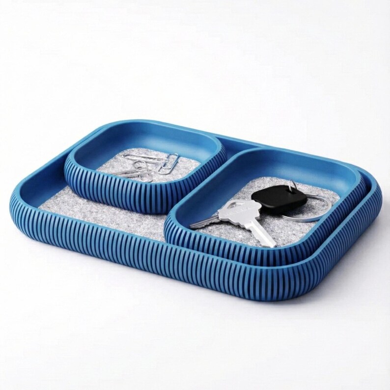 May include: A blue desk organizer with three compartments. The organizer has a ribbed exterior and a felt interior. One compartment holds paperclips, and another holds keys and a key fob. The organizer is designed to hold small items.