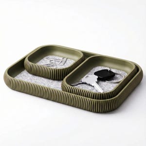 May include: Olive green desk organizer with three compartments. The organizer has a ribbed exterior and a gray felt interior. The compartments hold paperclips and keys. The organizer is designed to keep items organized.