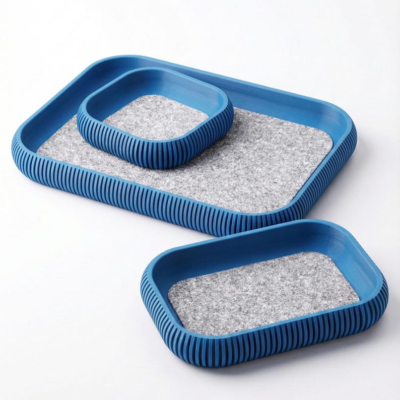 May include: Three blue rectangular trays of varying sizes. Each tray has a gray felt interior and a ribbed blue exterior. The trays are nested together, showcasing their different dimensions and design.