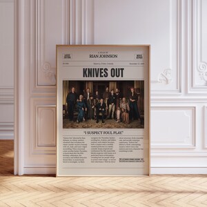 May include: A framed movie poster for "Knives Out" with a beige background and a group photo of the cast. The title is in large, bold letters. The poster includes text about the film's plot and credits.