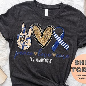 May include: Dark gray t-shirt with a peace sign, heart, and ribbon design in blue and gold, with the words "peace love ALS awareness". The shirt is a crew neck and has a simple, casual style.