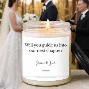 Puede incluir: Una vela encendida en un tarro de cristal con tapa negra. La etiqueta dice "Will you guide us into our next chapter?" con los nombres Jessica & Fred y la fecha 05.19.2026. El fondo muestra una ceremonia de boda.