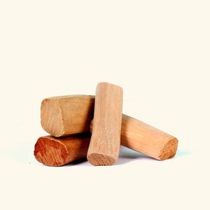 May include: Four pieces of sandalwood arranged on a white surface. The wood pieces are light brown with visible grain and cut ends. The pieces vary in size and shape, with a mix of cylindrical and rectangular forms.