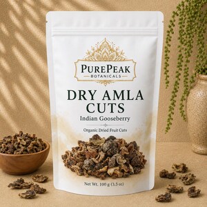 Puede incluir: Una bolsa blanca vertical de PurePeak Botanicals Dry Amla Cuts, también conocida como grosella espinosa india. La etiqueta presenta texto decorativo dorado y un gráfico de fruta seca. El peso neto es de 100 g. Se ven trozos de fruta seca.