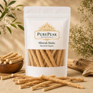 Op de afbeelding: Een witte stazak met lichtbruine Miswak-stokjes, gelabeld PurePeak Botanicals Natural & Organic. De zak heeft een doorzichtig venster met de houten stokjes, met extra stokjes verspreid op de voorgrond en een houten kom.