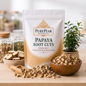 Peut inclure: Un sachet blanc debout étiqueté PurePeak Botanicals Papaya Root Cuts avec des accents dorés. Le sachet est entouré de petits bols en bois et d'une pelle en bois remplis de morceaux de racines botaniques séchées brun clair sur une surface en bois.