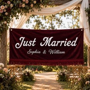 Könnte beinhalten: Ein weinrotes Samtbanner mit den Worten "Just Married" in weißer Schrift, darunter die Namen "Sophia & William". Das Banner hat einen Fransenbesatz am unteren Rand und wird bei einer Hochzeitszeremonie im Freien gezeigt.