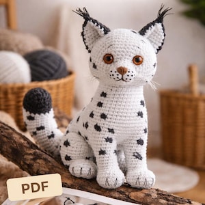 Op de afbeelding: Een gehaakte lynxwelp met wit garen, zwarte vlekken en bruine ogen zit op een houten tak. De tekst "Lynx Cub CROCHET PATTERN" staat bovenaan. Een PDF-pictogram staat in de linker benedenhoek. Een gehaakte lynxwelp staat op het open boek.