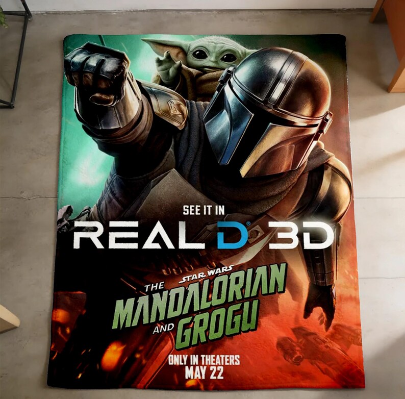 May include: A rectangular Star Wars themed blanket featuring The Mandalorian and Grogu. The blanket has a green, red, and orange background with the text "SEE IT IN REAL D 3D" and "ONLY IN THEATERS MAY 22".
