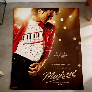 Op de afbeelding: Een rechthoekige deken met een portret van Michael Jackson. De afbeelding toont Jackson in een rode jas en een wit shirt met een pianotoetsenbordontwerp. De deken heeft de filmtitel "Michael" en andere tekst.