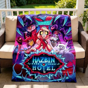 May include: A colourful blanket with a design featuring characters from Hazbin Hotel. The blanket has a dark blue border with the words "Hazbin Hotel" in a stylized font. The characters are in shades of red, purple, and white.