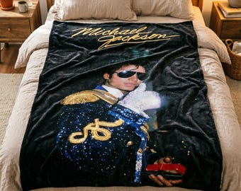 May include: A black plush throw blanket featuring a large graphic of Michael Jackson wearing a dark blue military-style jacket with gold embroidery, a white glove, and sunglasses. The text Michael Jackson is printed in gold script at the top.