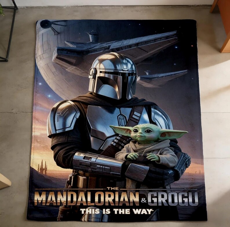 May include: A rectangular blanket featuring a scene from The Mandalorian. The image shows the Mandalorian holding Grogu, with a spaceship and planet in the background. The text "THE MANDALORIAN & GROGU THIS IS THE WAY" is at the bottom.