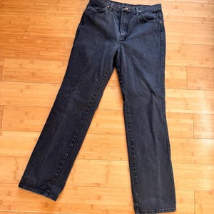 Może przedstawiać: Para dżins&oacute;w z ciemnego denimu z klasycznym pięciokieszeniowym designem. Dżinsy mają prosty kr&oacute;j nogawek i wysoki stan. Denim ma głęboki kolor indygo, a dżinsy leżą płasko na drewnianej powierzchni.