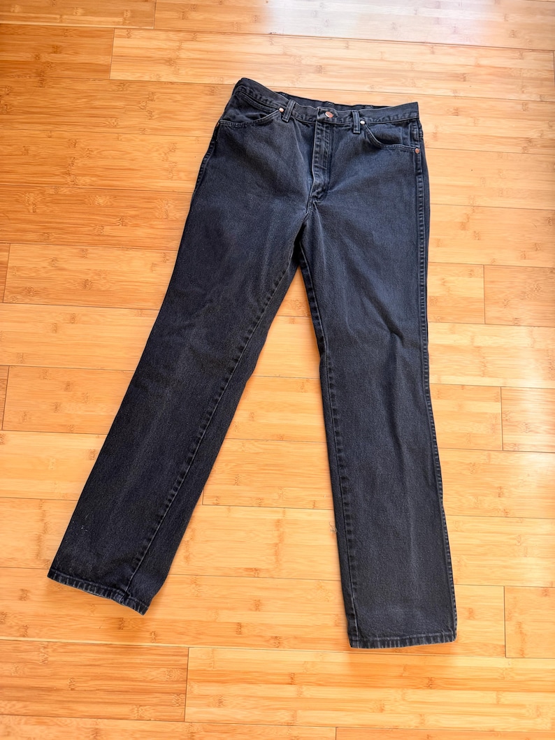 Może przedstawiać: Para dżins&oacute;w z ciemnego denimu z klasycznym pięciokieszeniowym designem. Dżinsy mają prosty kr&oacute;j nogawek i wysoki stan. Denim ma głęboki kolor indygo, a dżinsy leżą płasko na drewnianej powierzchni.