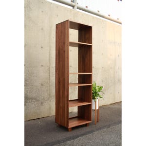 May include: A tall, wooden bookshelf with a dark brown finish. The bookshelf has multiple shelves of varying sizes and a rectangular shape. The shelves are open, and the bookshelf is standing on a concrete surface.