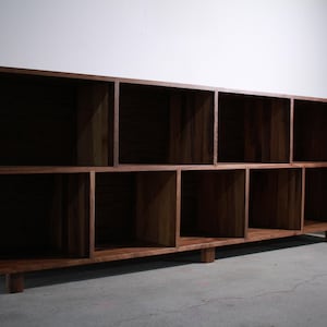 May include: A dark brown wooden bookshelf with ten cubbyhole compartments. The bookshelf is rectangular and sits low to the ground on short legs. A potted plant is visible in the background.