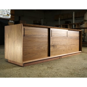 May include: A wooden cabinet with a natural finish and sliding doors. The cabinet is rectangular and made from wood, with visible grain. The design is simple and elegant, suitable for various storage needs. The cabinet is made from wood.