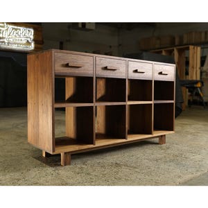 May include: A wooden storage cabinet with four drawers and eight open cubby spaces. The cabinet is made of a light brown wood and has a modern design. The drawers have simple, rectangular handles.