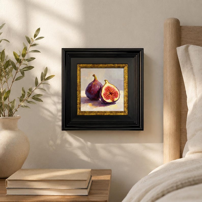 May include: A framed painting of two figs, one whole and one halved, revealing the red interior. The artwork is set against a light background, framed in black with a gold inner border. The painting is displayed on a wall.