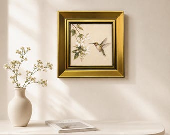 May include: A square framed painting featuring a hummingbird hovering near a branch of white blossoms. The artwork is encased in a wide, metallic gold frame with a dark inner border, showcasing detailed brushwork of the bird and flowers.