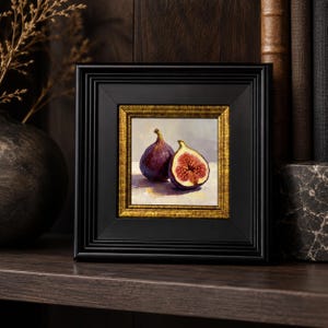 May include: A framed painting of two figs, one whole and one halved, showcasing a rich purple exterior and a vibrant red interior. The artwork is set within a black frame with a gold inner border, creating a classic aesthetic.
