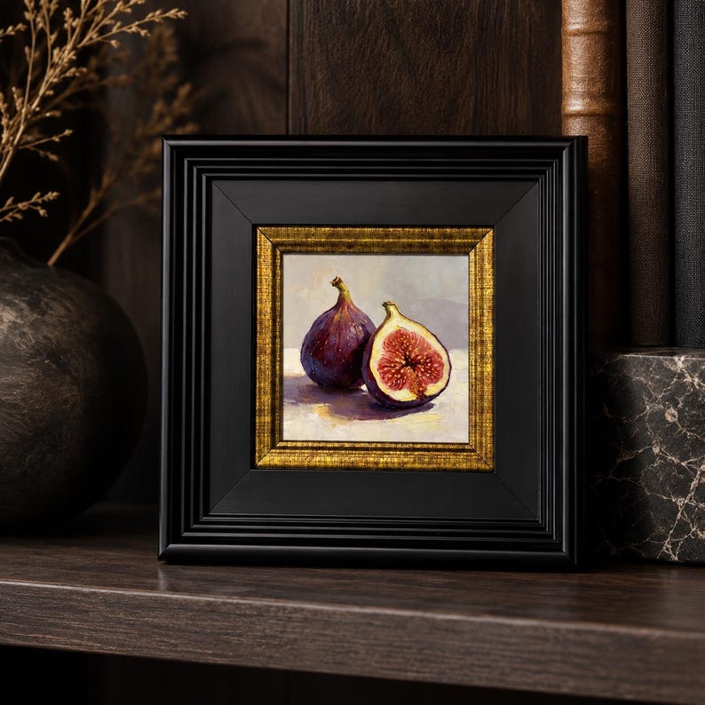 May include: A framed painting of two figs, one whole and one halved, showcasing a rich purple exterior and a vibrant red interior. The artwork is set within a black frame with a gold inner border, creating a classic aesthetic.
