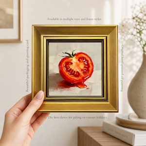 Könnte beinhalten: Ein quadratisches Ölgemälde einer aufgeschnittenen roten Tomate in einem dicken, verzierten Goldrahmen. Das Bild zeigt eine detaillierte, leuchtend rote Tomatenhälfte vor einem neutralen, strukturierten Hintergrund. Der Rahmen hat ein metallisches Gold-Finish.
