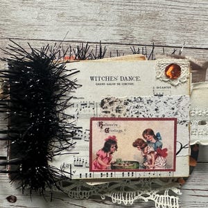 May include: A spiral-bound scrapbook featuring a vintage sheet music cover titled Witches' Dance. The cover includes a rectangular illustration of two children, a piece of white lace, and a thick fringe of black tinsel along the left side.