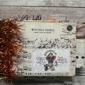 May include: A rectangular journal featuring a cover with vintage sheet music titled Witches' Dance, accented by orange tinsel, a lace patch, and a central illustration of a witch with a cat and owl, accompanied by the text Halloween and poetic verses.