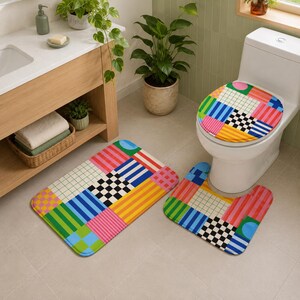 May include: A bathroom set consisting of a toilet seat cover, a rectangular bath mat, and a U-shaped contour mat. Each piece features a vibrant, multi-colored geometric pattern with squares, stripes, checkerboard motifs, and solid color blocks.
