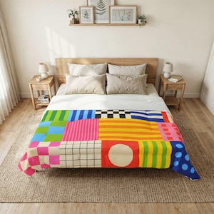 May include: A bedspread featuring a vibrant patchwork design of various geometric patterns including stripes, checkers, grids, and polka dots in bright colors like red, yellow, blue, green, and pink, covering a bed with four neutral-toned pillows.