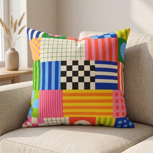 Könnte beinhalten: Ein quadratisches Zierkissen mit einem lebendigen Patchwork-Design aus verschiedenen geometrischen Mustern. Die Oberfläche zeigt eine Mischung aus farbigen Gittern, vertikalen und horizontalen Streifen sowie einem zentralen schwarz-weißen Schachbrettmuster.