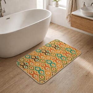 Puede incluir: Una alfombra de baño rectangular con un patrón retro en tonos marrón, naranja, verde y amarillo. El diseño presenta formas ovaladas repetidas y pequeños detalles en forma de estrella. La alfombra está colocada sobre un suelo de madera clara.