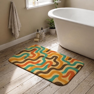 Può includere: Un tappetino da bagno rettangolare caratterizzato da un motivo ripetitivo di linee ondulate e interconnesse nei toni del verde acqua, giallo senape, arancione e marrone scuro. Il tappetino presenta angoli arrotondati e una consistenza morbida.