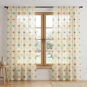May include: Sheer off-white curtains featuring a repeating pattern of multi-colored starbursts and small dots in shades of teal, orange, olive green, and brown. The curtains are hung on a black rod and cover a window with a wooden frame.