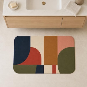 May include: A rectangular bath mat featuring a geometric pattern of solid color blocks in navy blue, cream, terracotta red, mustard yellow, dusty pink, and olive green. The design consists of rounded shapes and straight vertical lines.